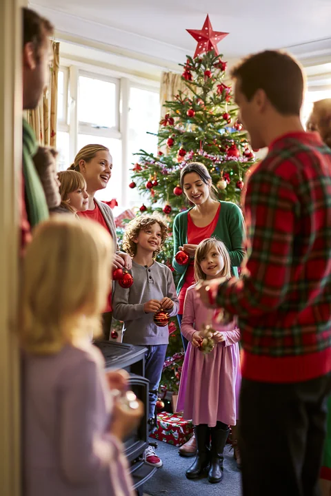 A family is singing Christmas carols together indoors, surrounded by festive decorations and a Christmas tree.