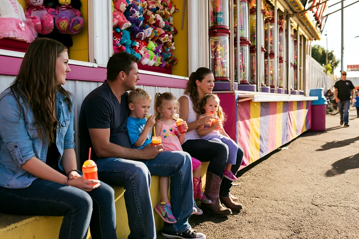 A family sits together at a fairground, holding snacks and enjoying the atmosphere.