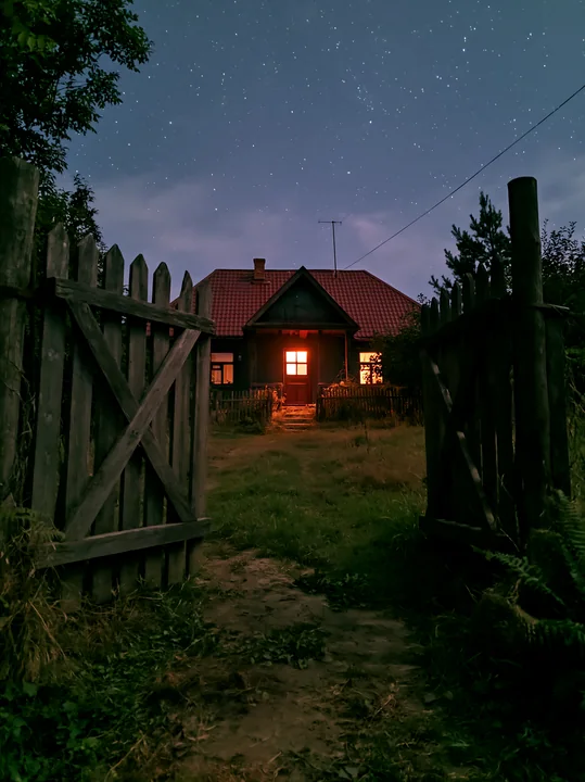 A farmhouse stands under a clear night sky filled with stars.