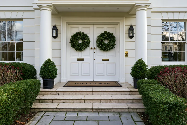 A front door with wreath and welcome doormat stands in a well-maintained residential area.