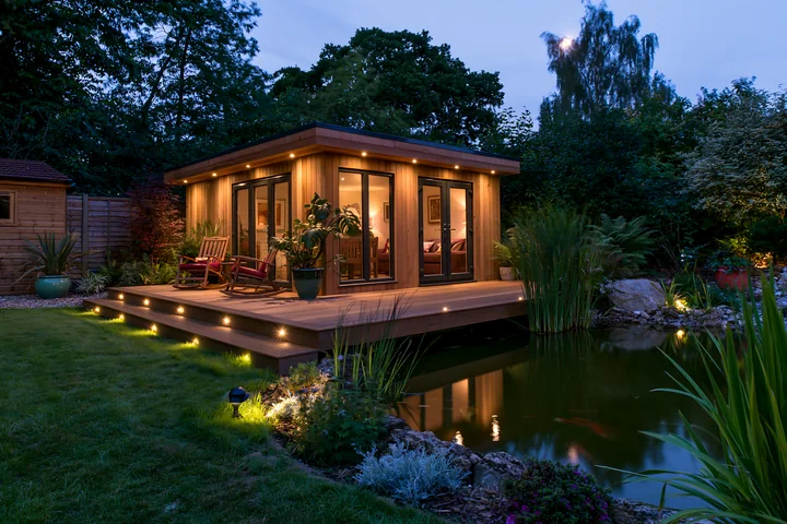 A garden room features large windows and a deck that is illuminated.