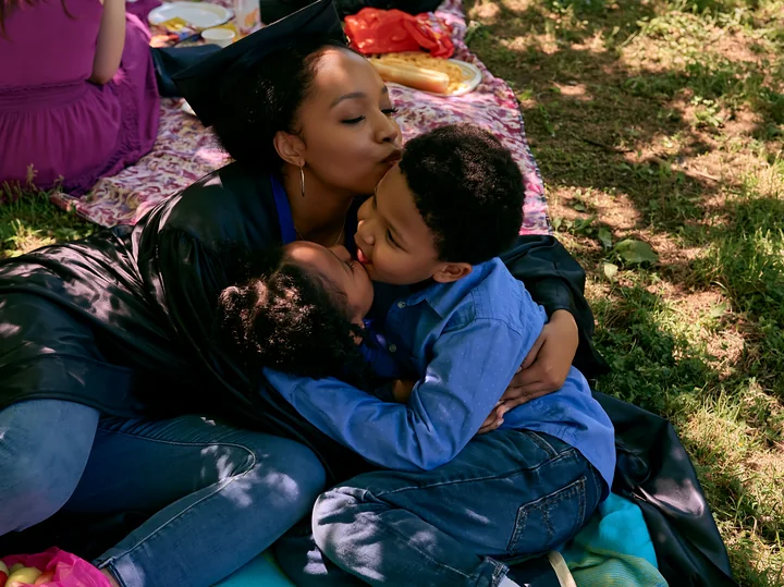 A graduate shares a moment with her children during a graduation celebration in a park.