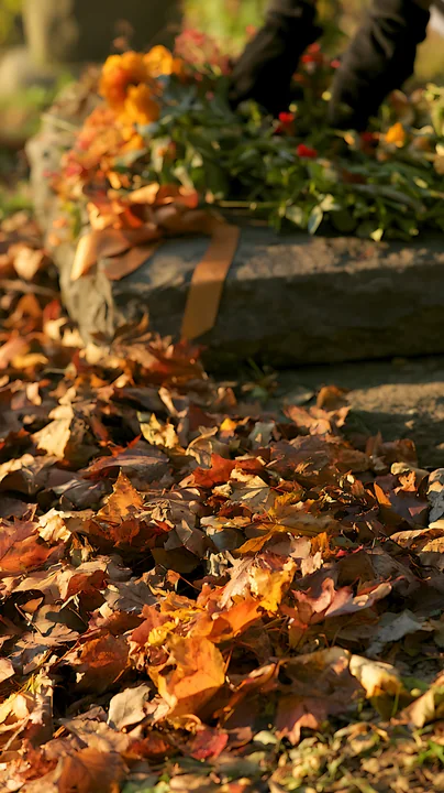A grave with a mourning ribbon and flowers surrounded by fallen autumn leaves.