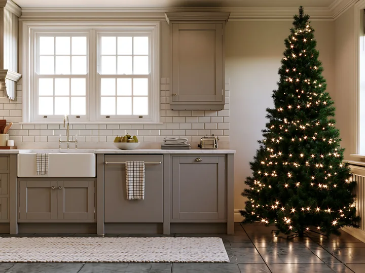 A holiday decorated kitchen showcases an illuminated Christmas tree beside a sink and countertops.
