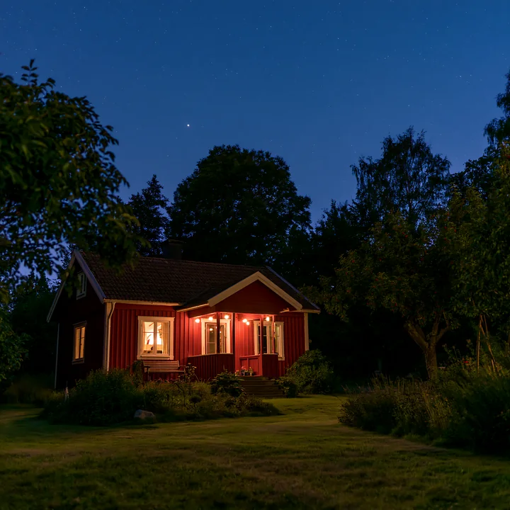 A house sits under a starry sky with warm lights glowing from the windows.