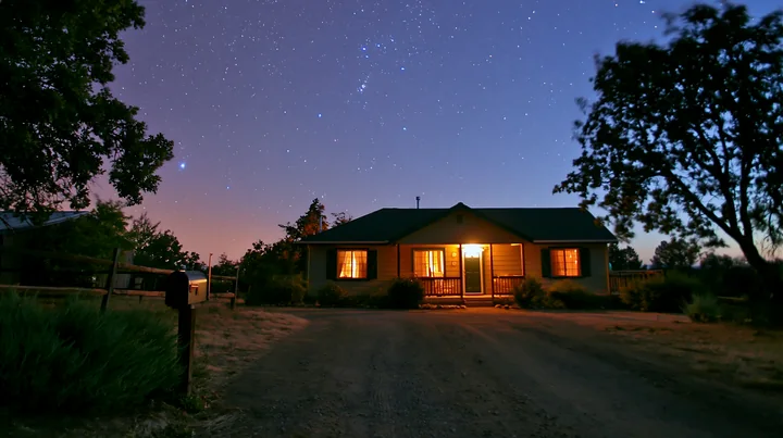 A house stands under a starry sky, with lights glowing from the windows.