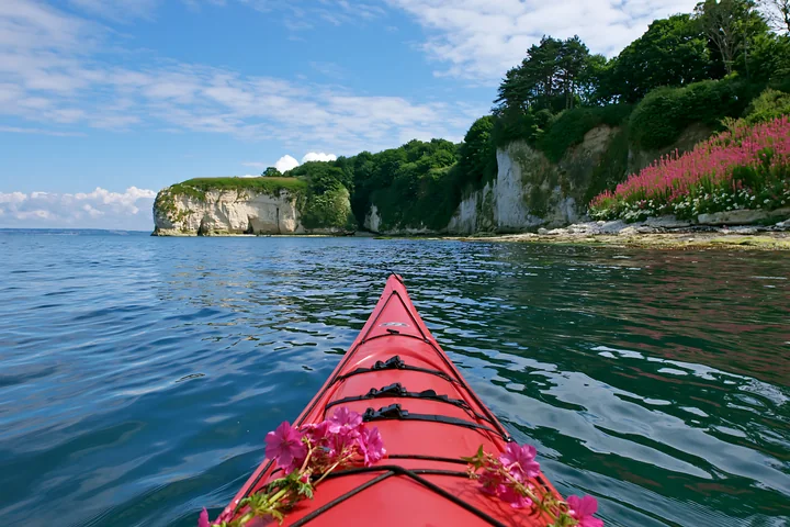 A kayak shows colorful flowers along the water's edge of an island with flowers and white cliffs under a bright sky.