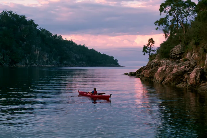 A kayaker paddles through calm waters in a sheltered bay surrounded by a rocky coastline.