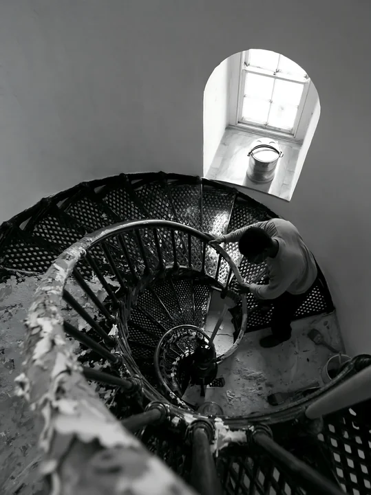 A lighthouse maintenance worker at work repairs equipment while standing on a spiral staircase.