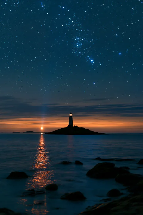 A lighthouse stands on an island under a starry night over a calm ocean.