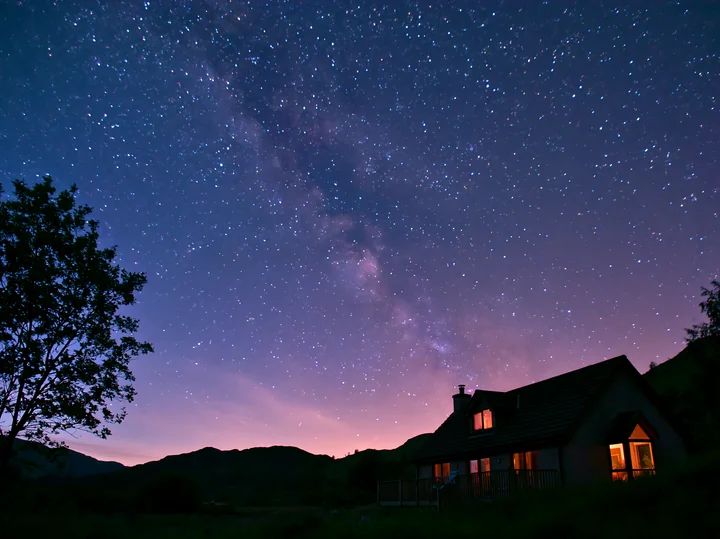 A modern house sits under the Milky Way as stars fill the night sky.