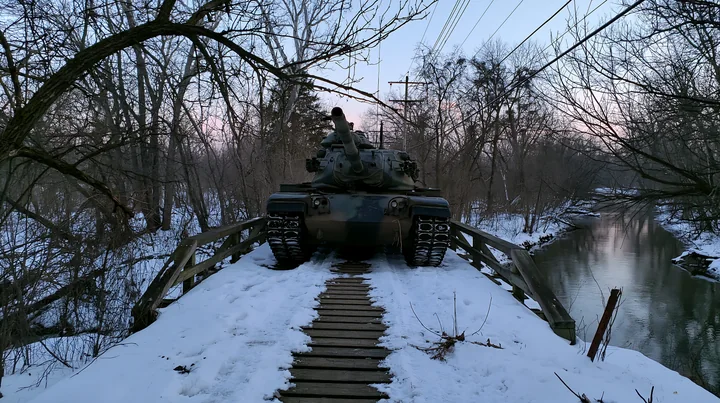 A panzer tank in winter snow sits on a wooden bridge above a creek.