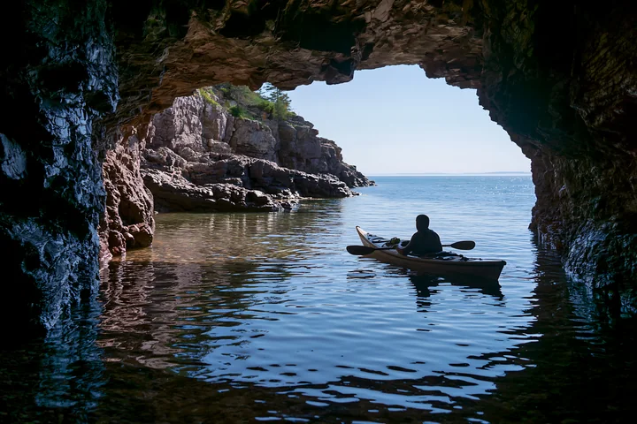 A person in a kayak explores a sea cave, looking out at the coastline.