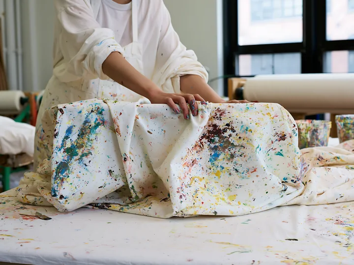 A person is handling cotton fabric covered in various colors of paint in a workspace.