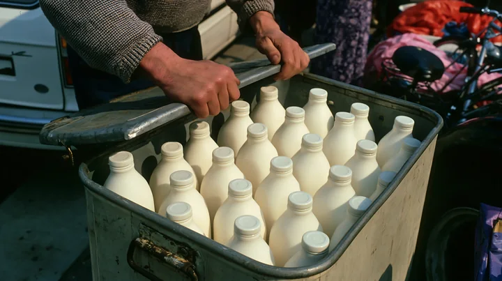 A person opens a metal market cooler filled with cold milk bottles at a bustling market.