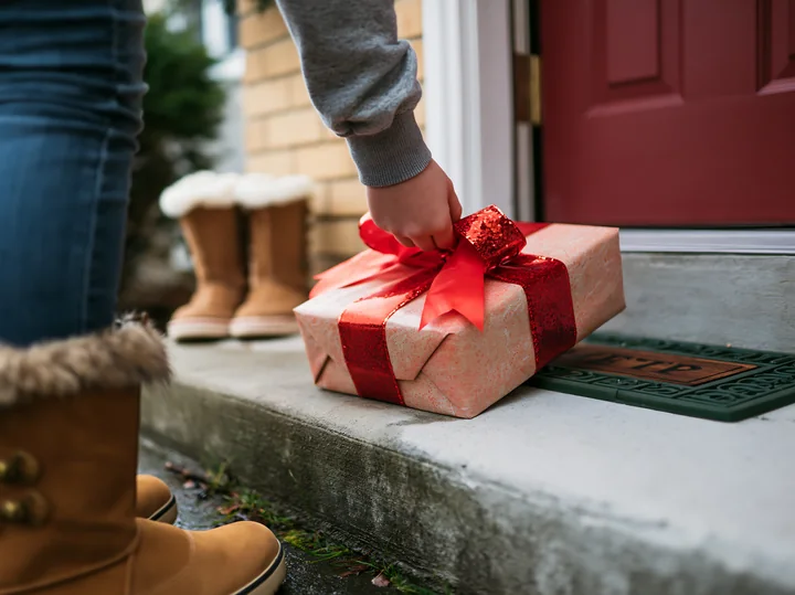 A person places a wrapped gift with a red bow on a doorstep.