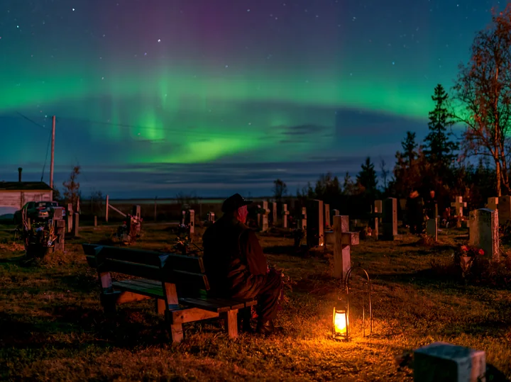 A person sits on a bench in a military cemetery under the northern lights.