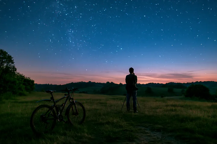 A person stands with a tripod looking at the starry sky in a rural area.