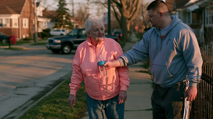 A person with Parkinson's disease receiving support from a caregiver while walking on a neighborhood street.