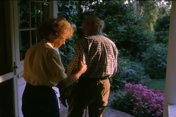 A person with Parkinson's disease receiving support from another individual in a garden during late afternoon.
