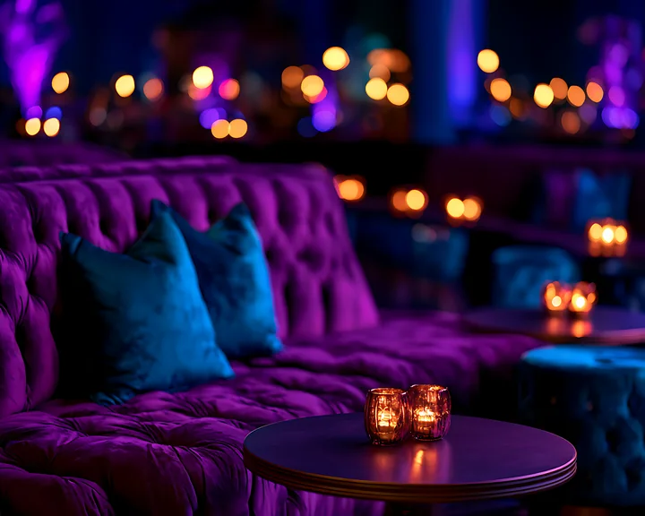 A plush couch and small tables are set in a lounge area with soft purple and blue lighting.