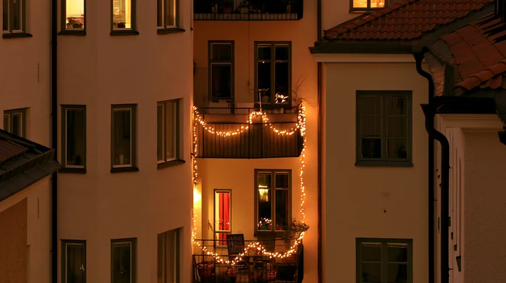 A residential balcony decorated with warm Christmas lights shines in the evening.