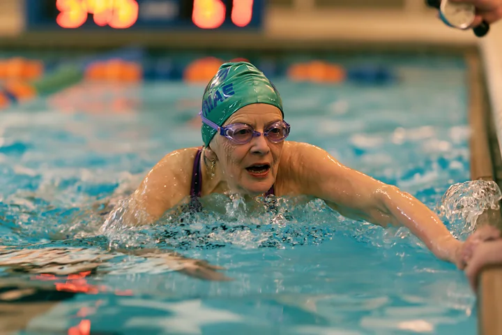 A senior woman swims freestyle in a lap pool, focusing on her technique as she glides through the water.