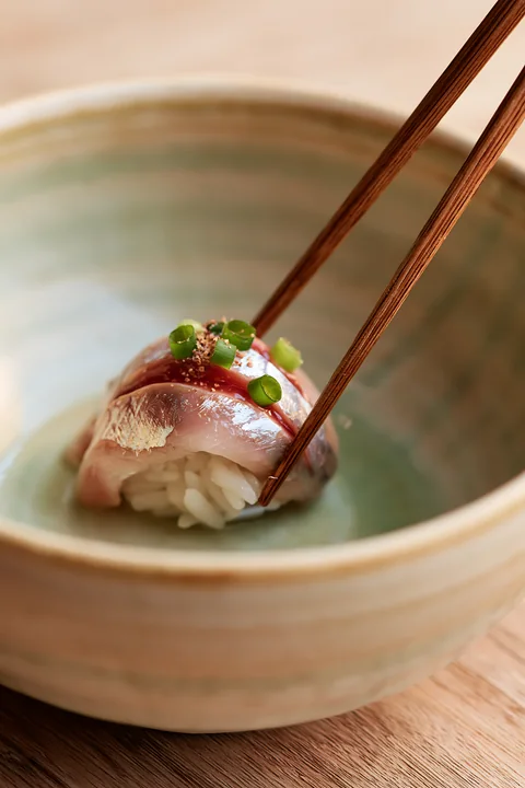 A single sushi piece ready to eat with chopsticks sits in a ceramic bowl.