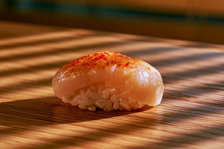 A single sushi piece rests on a light wooden table.