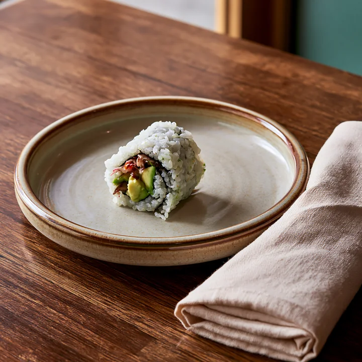 A single sushi roll on ceramic plate resting on a wooden table.