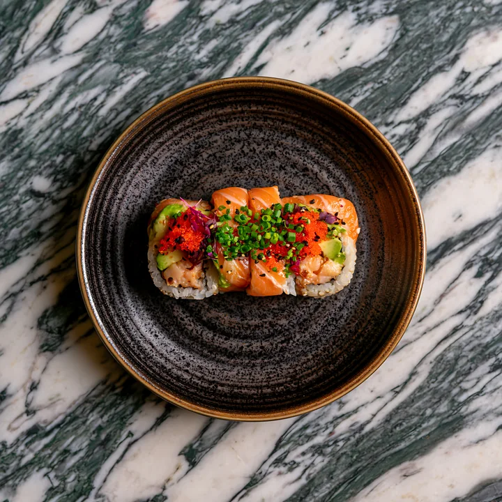 A single sushi roll on ceramic plate sits on a marble tabletop.