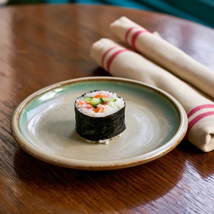 A single sushi roll on ceramic plate sits on a wooden table.