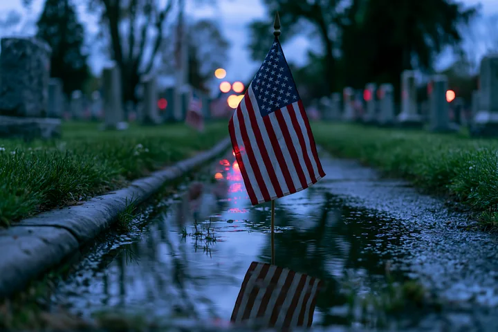 A small American flag stands in a puddle at a veterans cemetery at dusk.