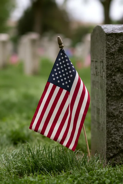 A small American flag stands next to a grave marker at Arlington cemetery.