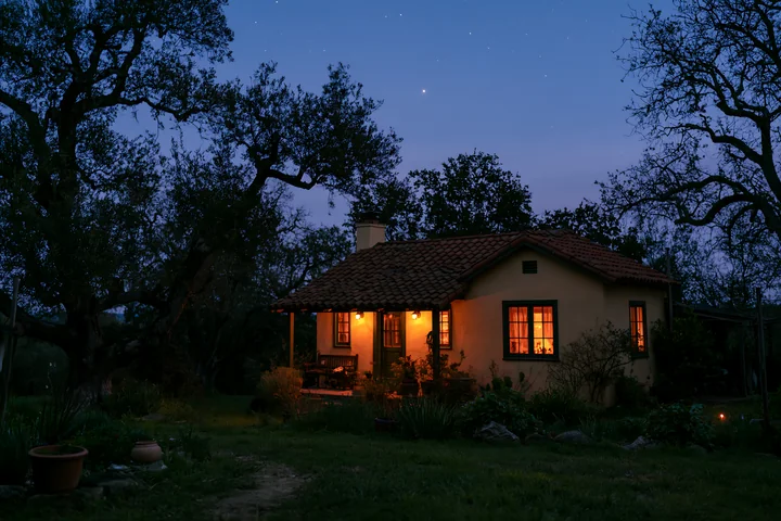 A small house stands under stars during blue hour, lit by warm lights.