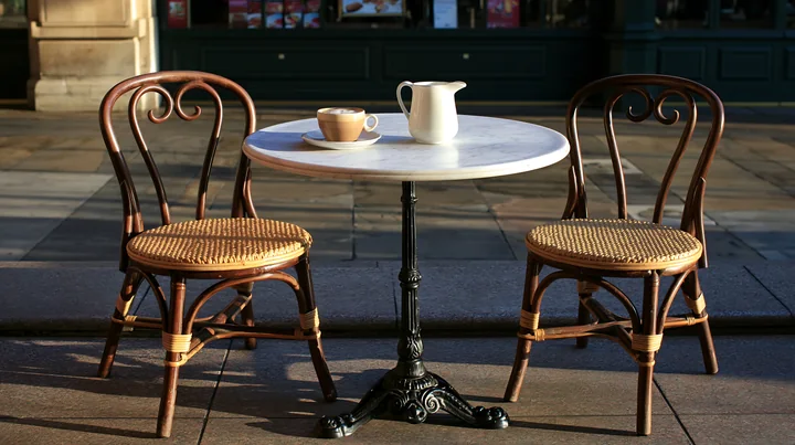 A small outdoor cafe table is set on a sidewalk with a latte and a milk jug.