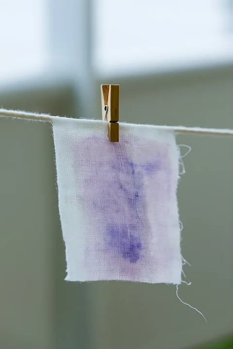 A small piece of muslin fabric with a watercolor stain in purple hangs on a clothesline.