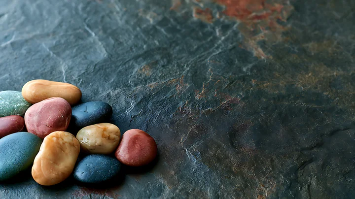 A small pile of smooth, colorful pebbles rests on a textured dark stone surface.