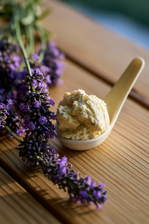 A small scoop of cream sits in a spoon beside fresh lavender flowers on a wooden table.