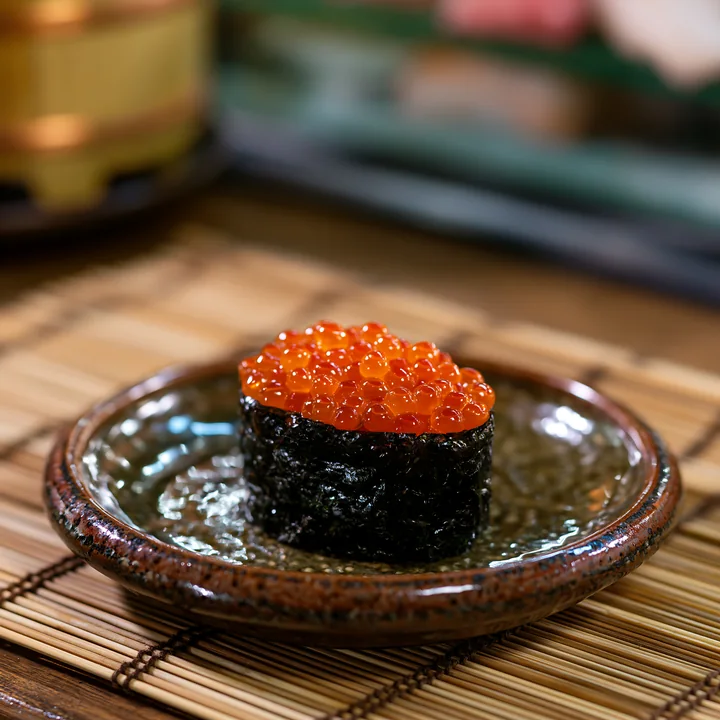 A small serving of ikura salmon roe sushi sits on a round plate.