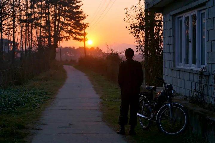 A soldier silhouette at dawn stands beside a bicycle on a quiet path.