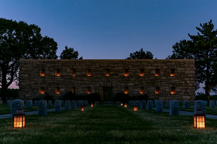 A soldiers' cemetery is illuminated by lanterns, showing headstones aligned in rows.