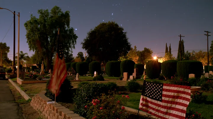 A solemn cemetery with an American flag waving in the breeze under a starlit sky.