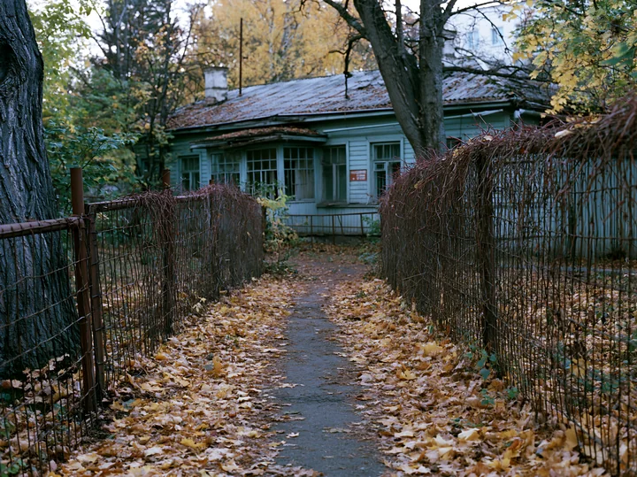 A Soviet abandoned building stands surrounded by a pathway covered in fallen leaves.