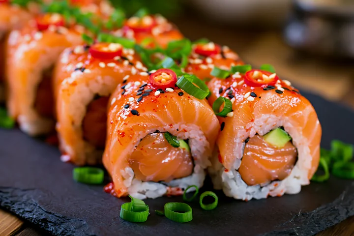 A spicy salmon sushi roll with chili is arranged neatly on a dark plate.