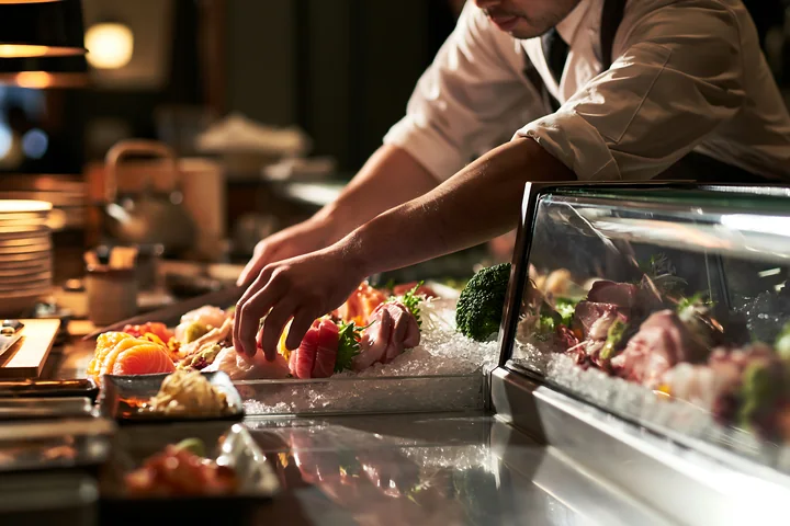 A sushi chef arranges sashimi on an ice display at a restaurant counter.