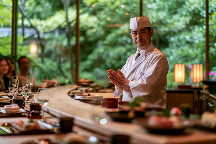 A sushi chef greeting diners in a restaurant with a warm smile.