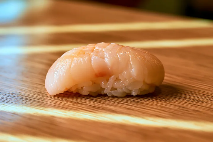 A sushi piece rests on a wooden table, highlighting its simple design.