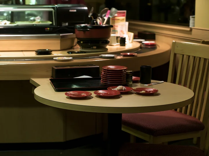 A table in a sushi conveyor belt restaurant shows several empty red plates stacked up.