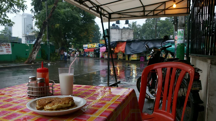 A table set for breakfast features pancakes and a glass of milk, while rain falls outside.